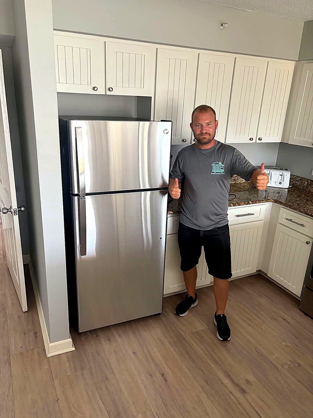 Beach House Moving crew member beside a newly installed stainless refrigerator in a Destin condo