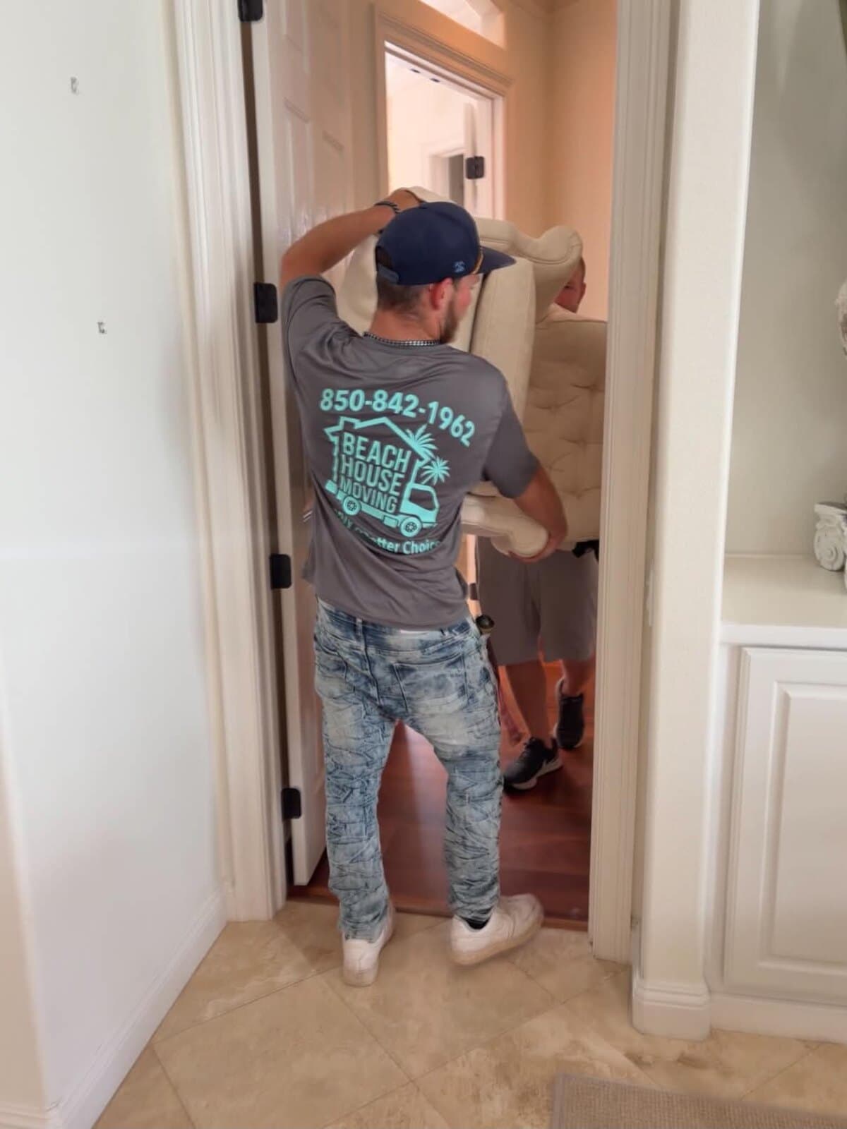 Two Beach House Moving movers angling a tufted armchair through an interior doorway in Destin