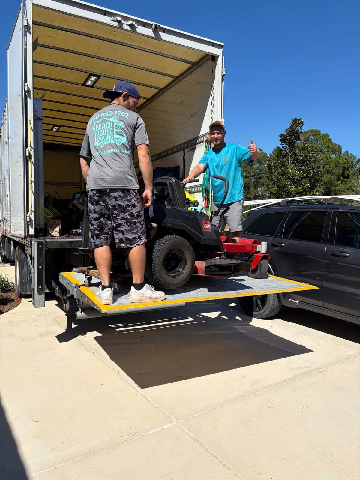 Beach House Moving crew with a red zero-turn mower on the raised box truck lift gate in Hammock Bay, Freeport, FL