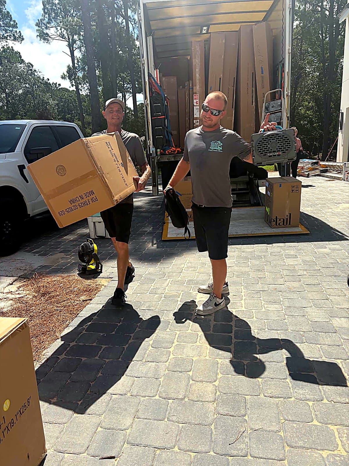 Beach House Moving crew unloading flat-packed furniture from a box truck lift gate
