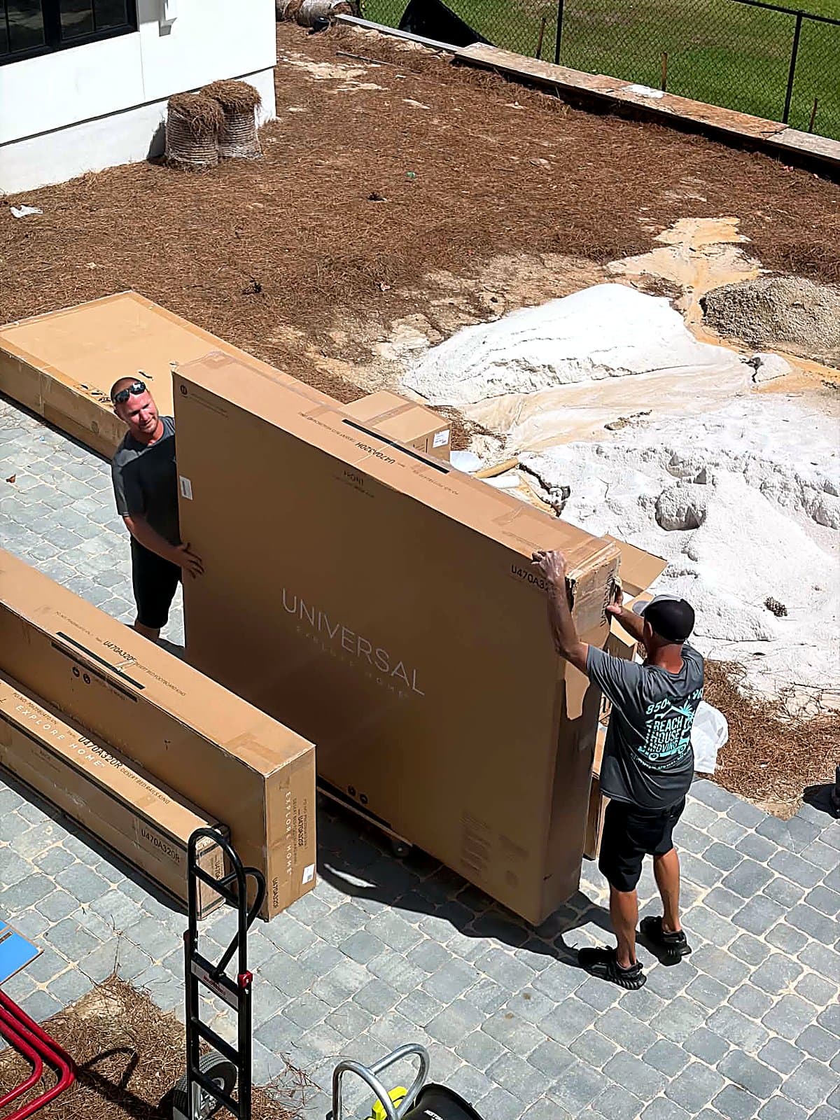 Beach House Moving crew lifting a king headboard box off a furniture dolly