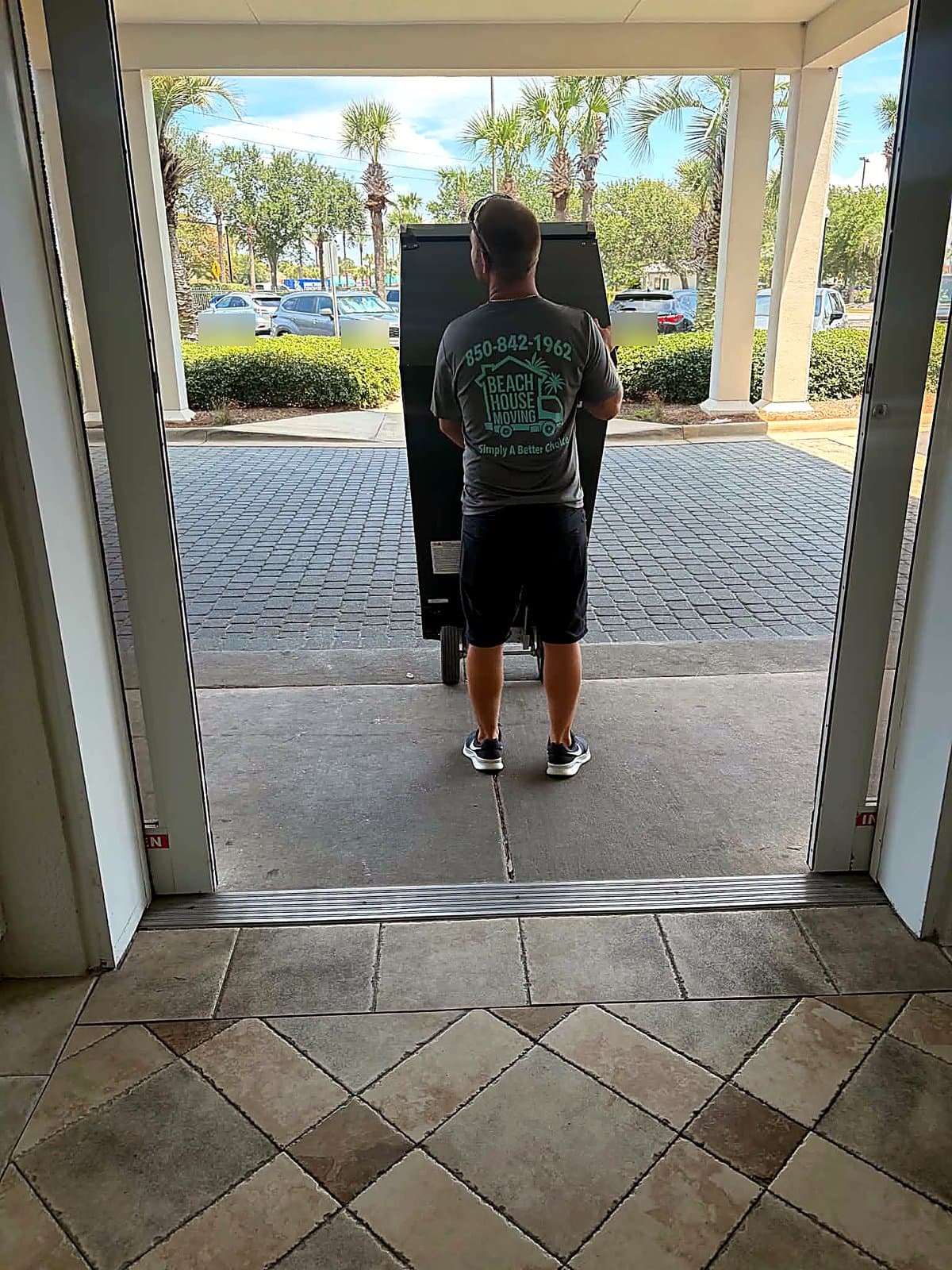 Beach House Moving crew wheeling a refrigerator on a hand truck out of a Destin condo tower