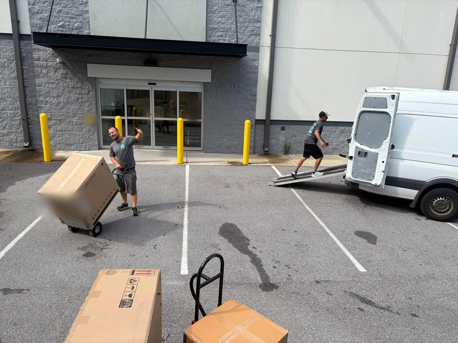 Beach House Moving crew with a hand truck and boxed furniture outside a storage facility entrance, with a van and its ramp behind