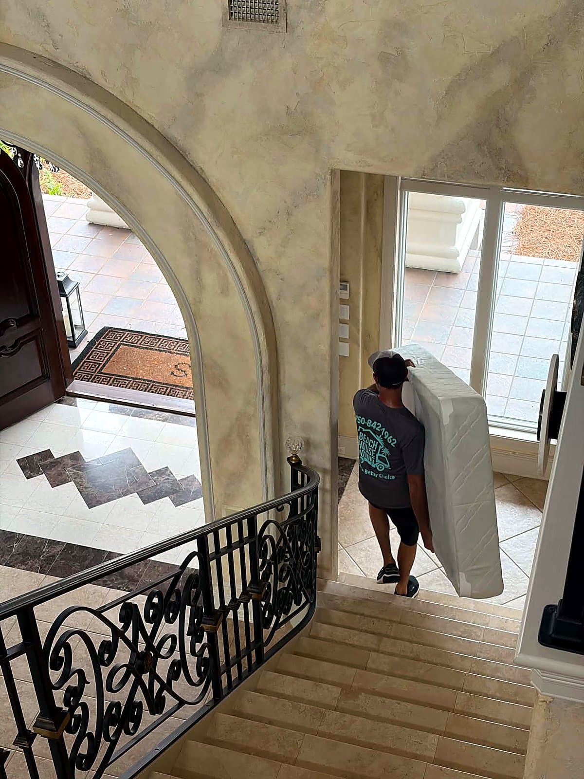Beach House Moving crew member carrying a box spring through a luxury home