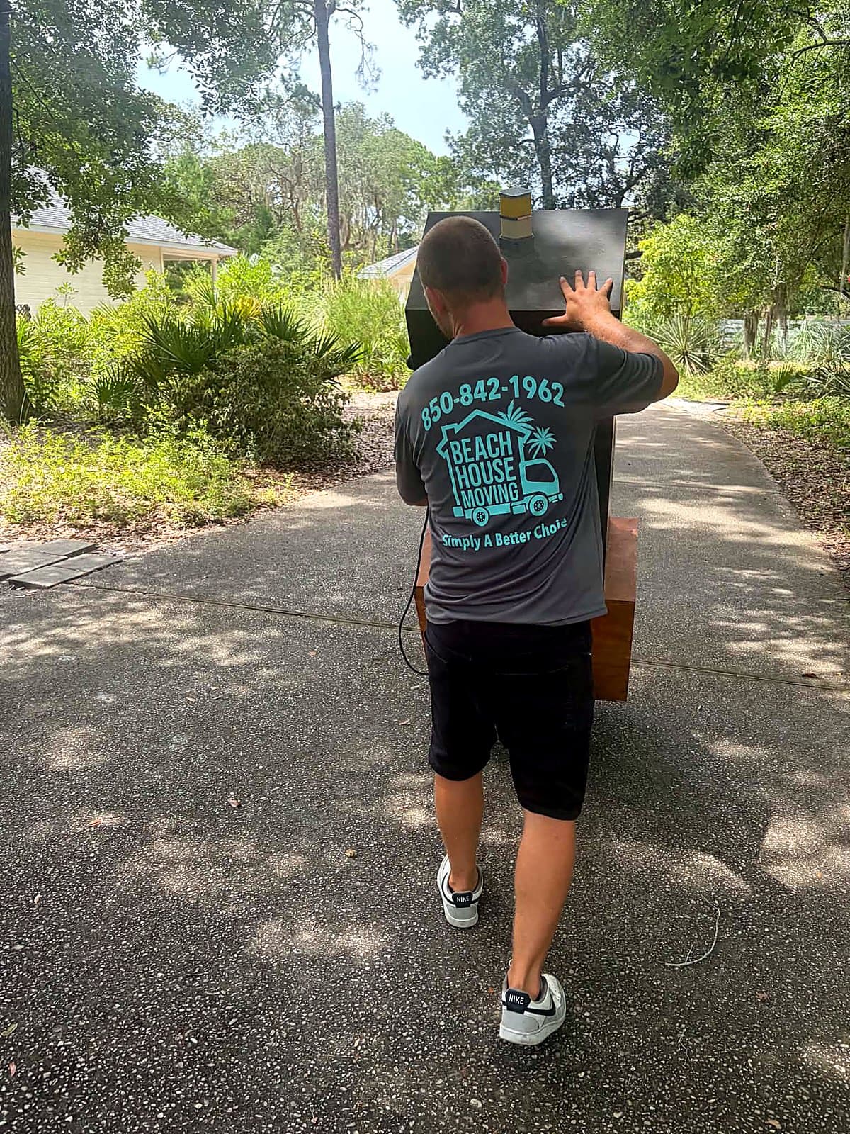 Beach House Moving crew member in branded shirt carrying a specialty item up a driveway on 30A