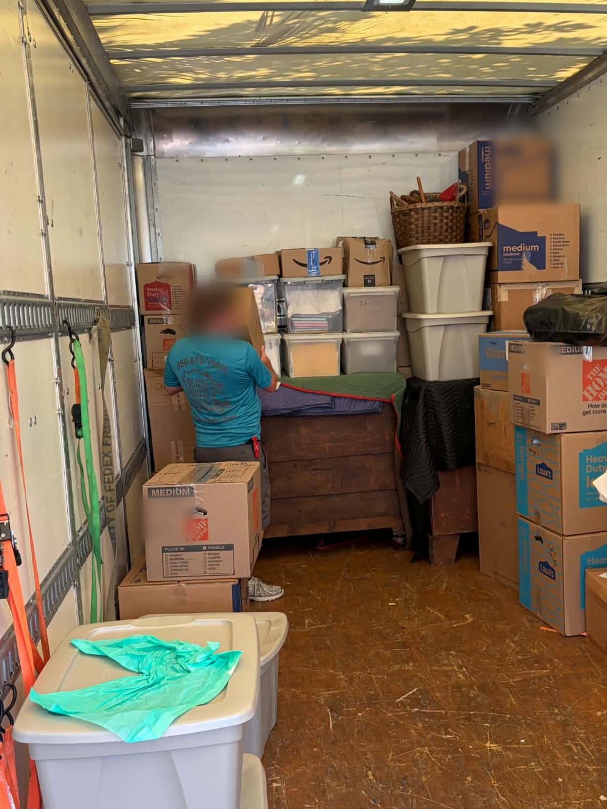 Inside a Beach House Moving truck: bins and boxes stacked on a padded wood chest, strapped to the wall rails