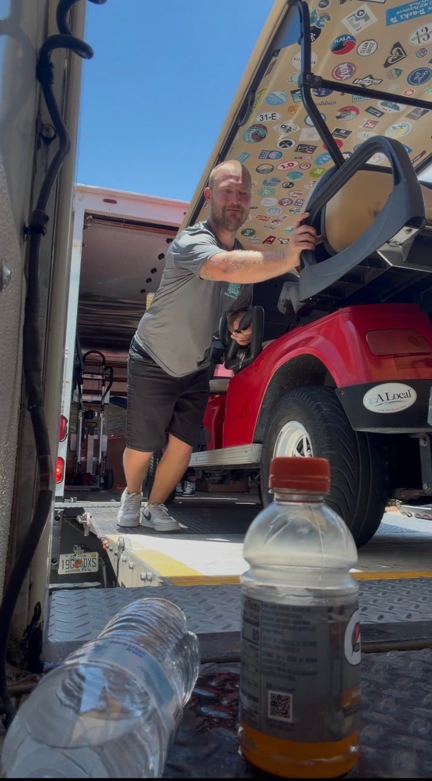 Beach House Moving crew loading a red golf cart onto a box-truck lift gate during a 30A move