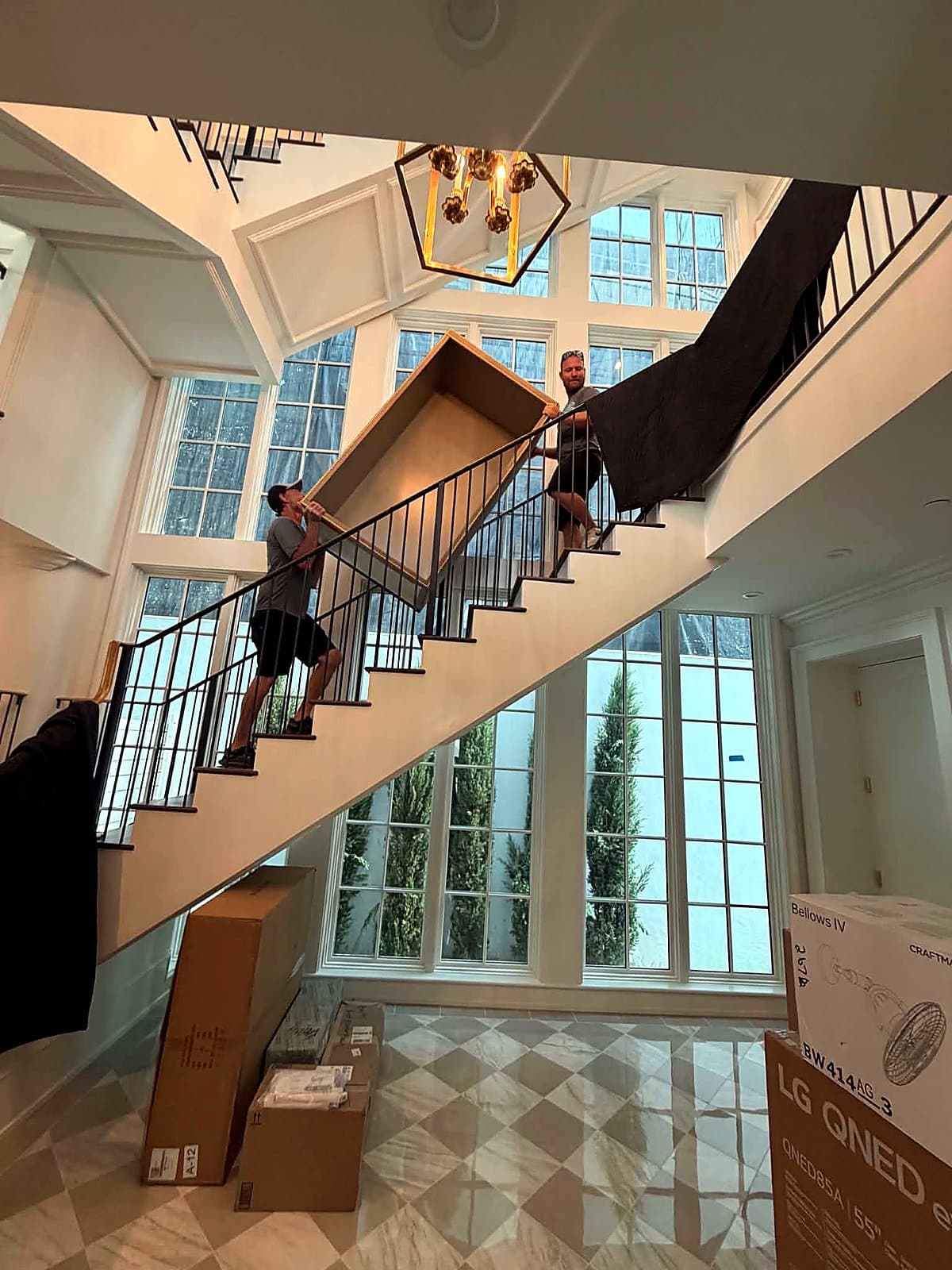 Beach House Moving owners carrying a large framed mirror up a staircase during a luxury new-construction move-in on 30A