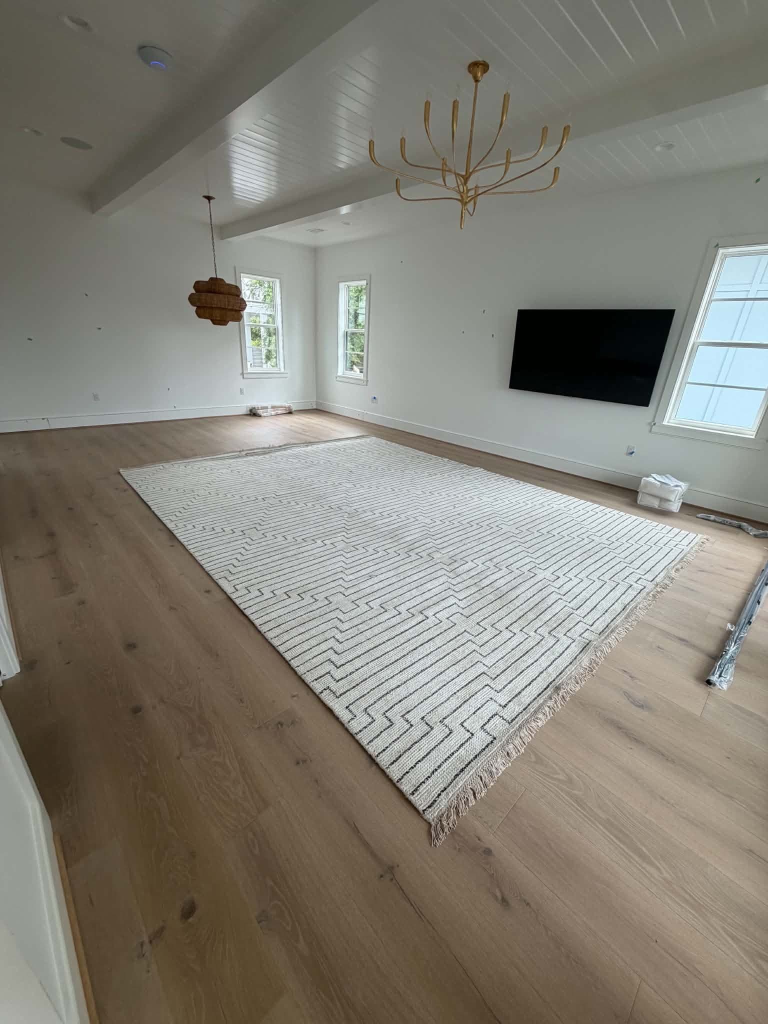 Beach House Moving laying the rug in an empty new-construction great room with a vaulted shiplap ceiling on 30A