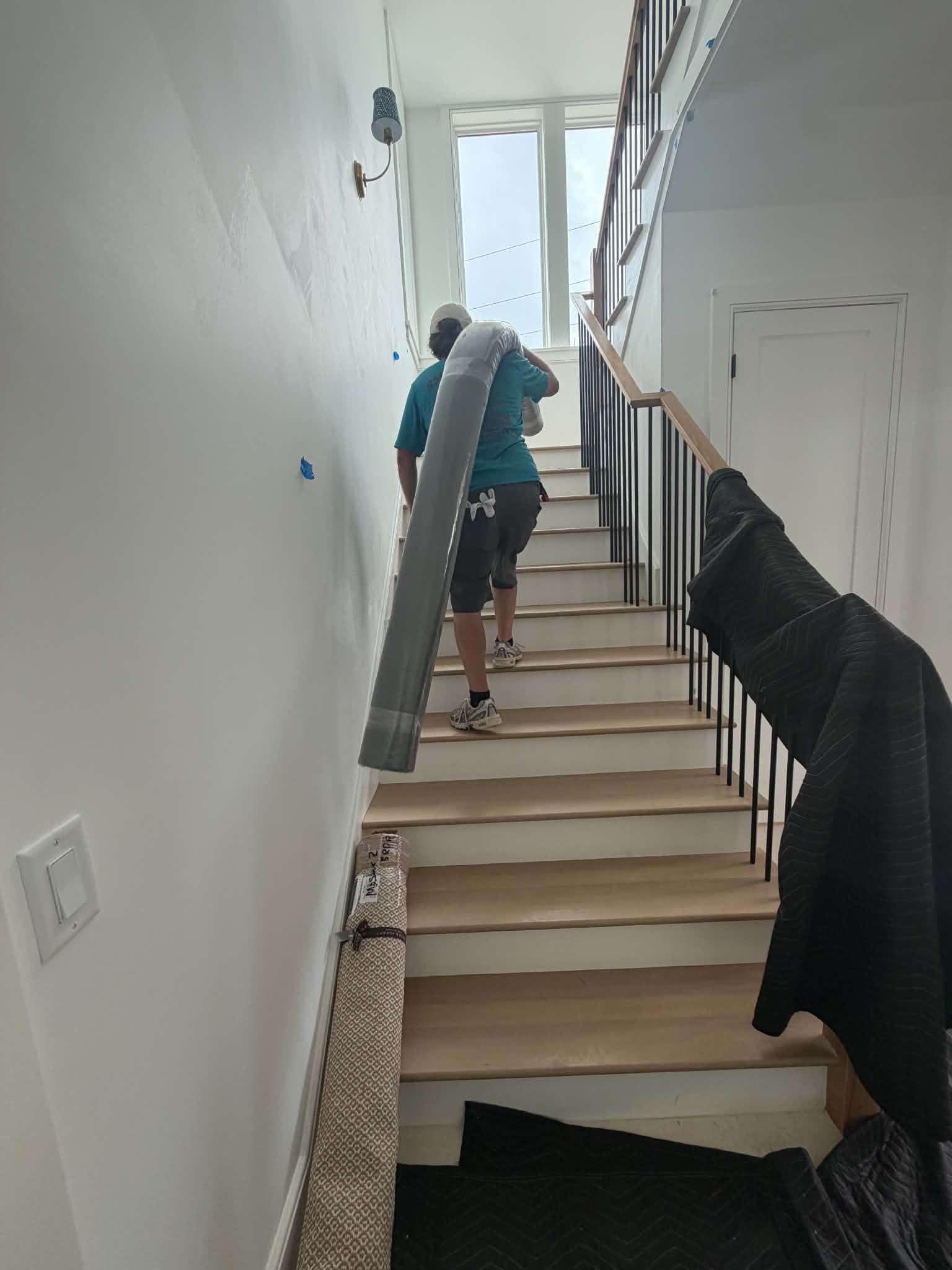 Beach House Moving crew member carrying a rolled wool rug up the stairs of a new-construction beach home on 30A