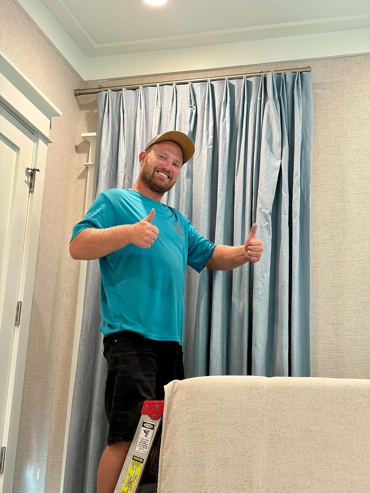 Beach House Moving mover Zack beside finished drapery panels in a Santa Rosa Beach, FL primary bedroom on a Tracery Interiors job